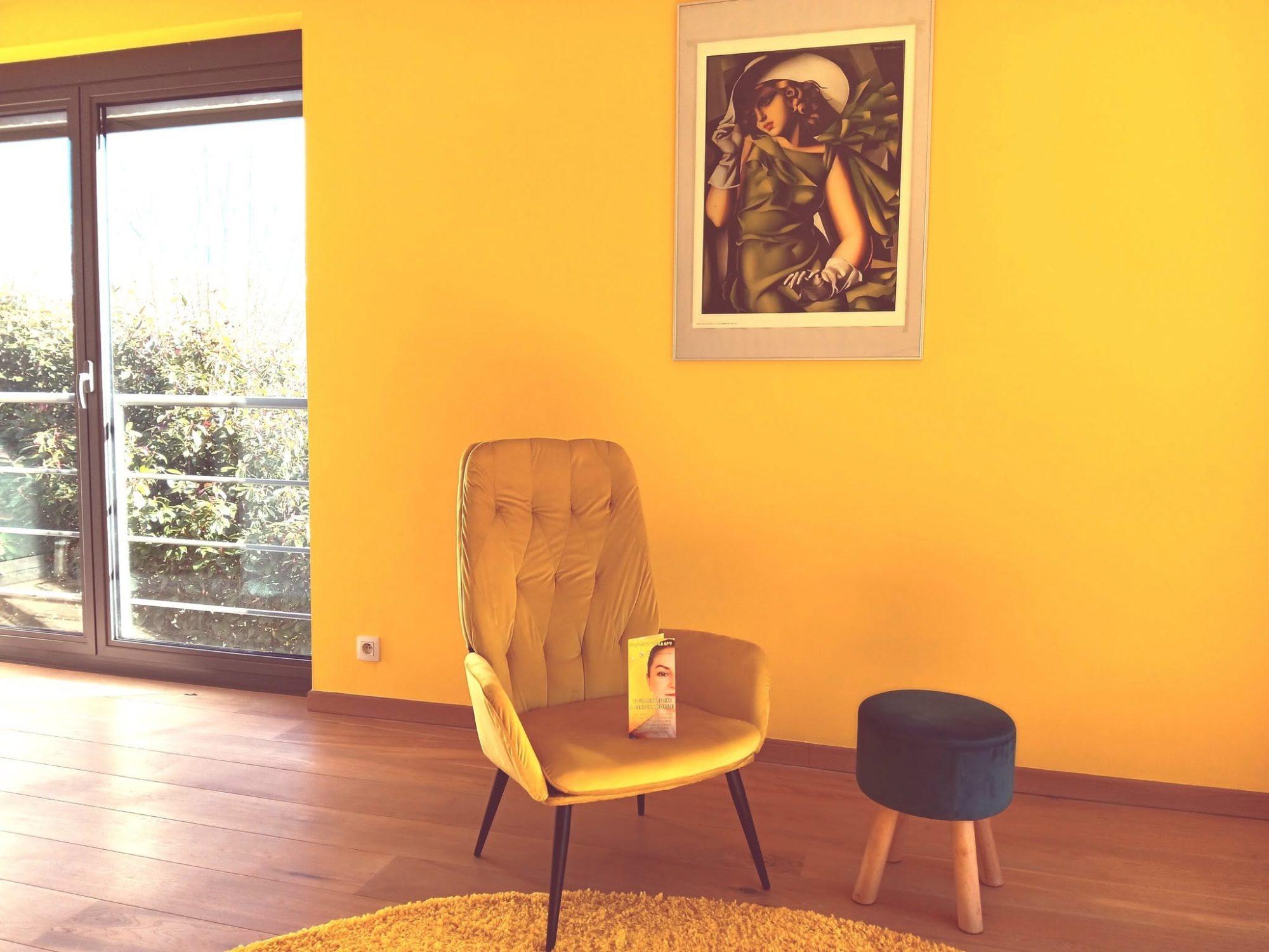 De zonnige praktijkruimte van Sunlight Therapy, met gele muur, planten en een zachte zetel